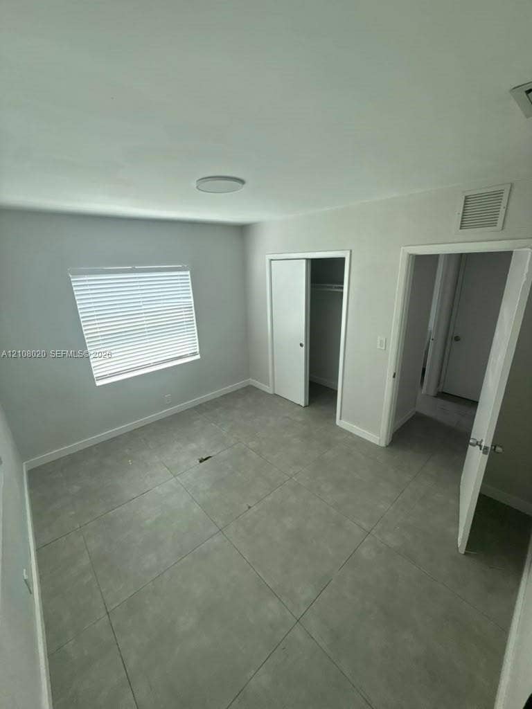 Large-format neutral tile flooring, window with installed blinds, and built-in closet storage