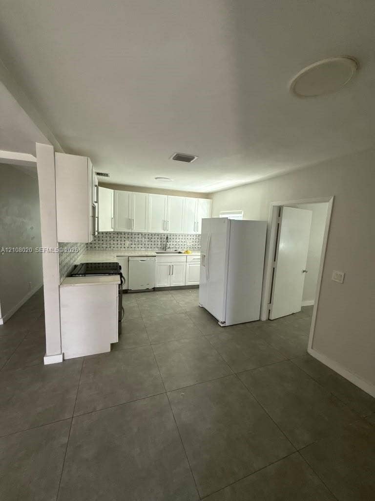 Kitchen featuring white shaker-style cabinetry, patterned tile backsplash, large-format tile flooring, and white built-in appliances