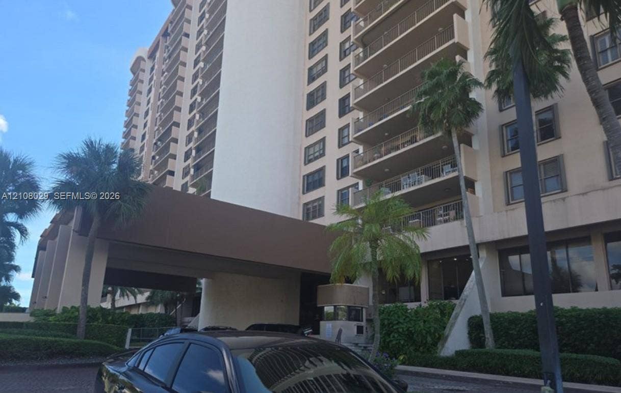1800 NE 114th Street, #2207, Miami, FL 33181 Multi-story high-rise exterior featuring a covered entryway, private balconies, and landscaped tropical plantings