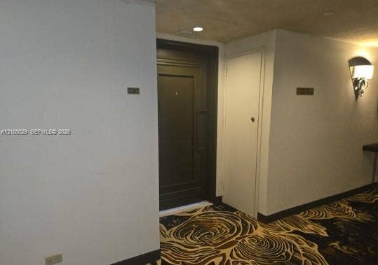 1800 NE 114th Street, #2207, Miami, FL 33181 Entryway featuring a dark-finish panel door, recessed ceiling lighting, wall-mounted light fixture, and patterned carpet flooring