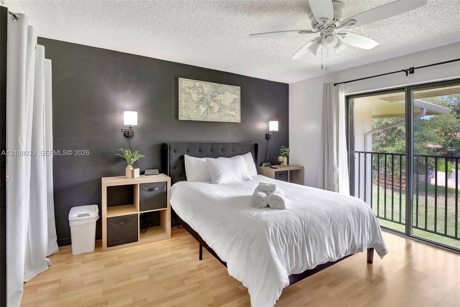 5821 Washington Street, #30, Hollywood, Hollywood, FL 33023 Bedroom featuring wood-finish flooring, a dark accent wall, two wall-mounted light fixtures, a ceiling fan, and sliding glass doors leading to a balcony