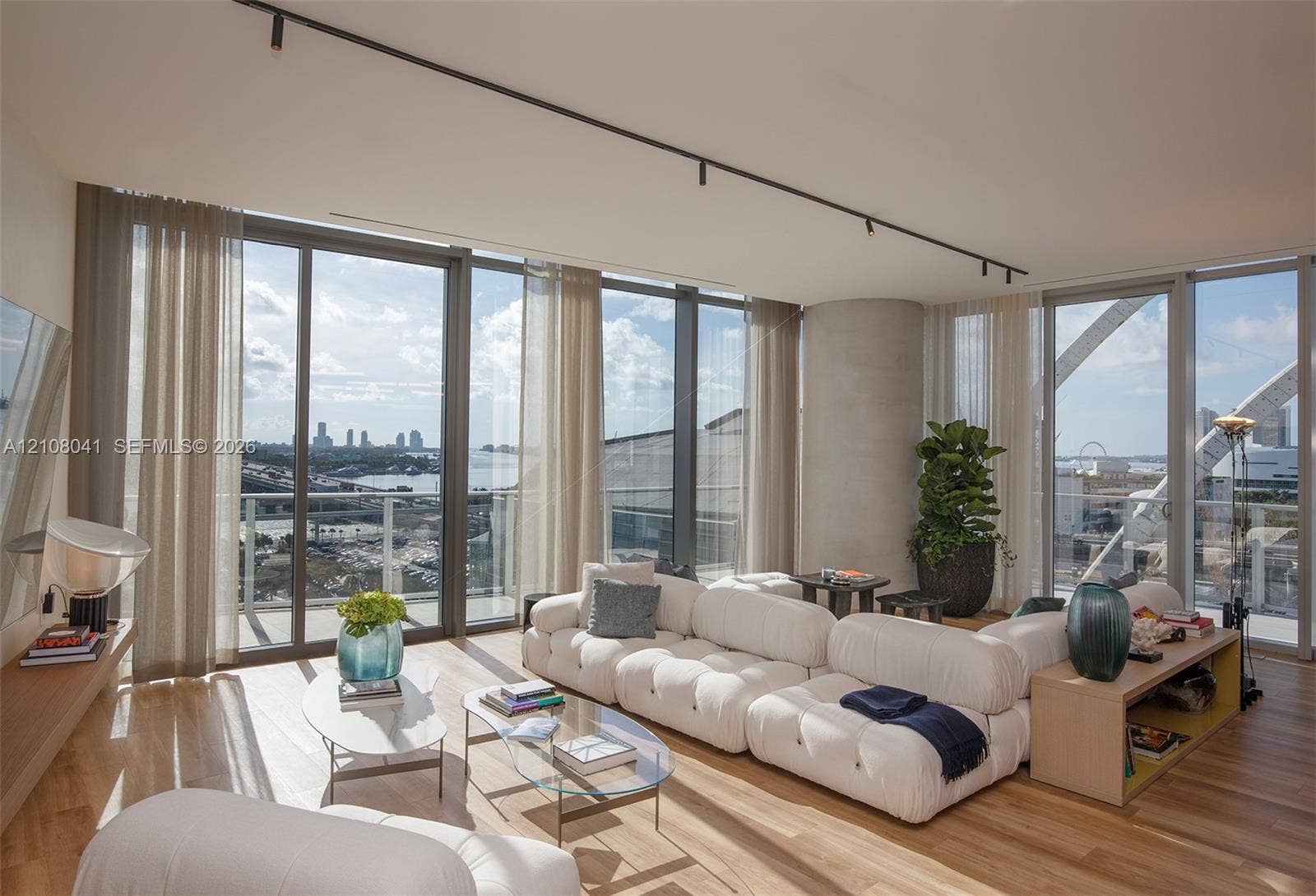 Expansive windows with city and water scenery, light wood-finish flooring, and track lighting