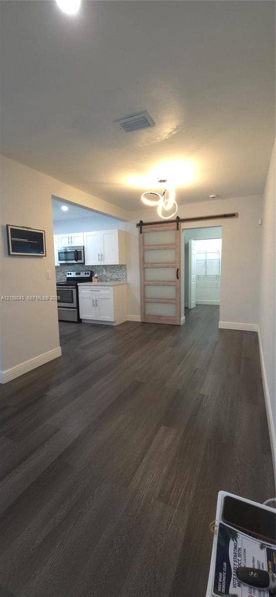 7176 SW 12th Street, #7176, Miami, Miami, FL 33144 Wood-finish flooring, sliding glass-panel barn door with metal hardware, contemporary three-ring light fixture, white kitchen cabinetry, and stainless steel kitchen appliances