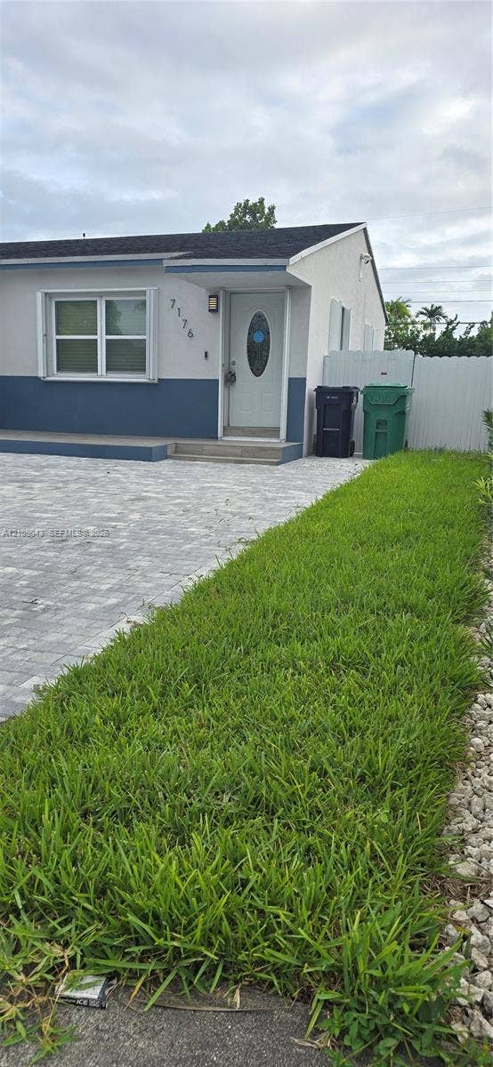 7176 SW 12th Street, #7176, Miami, Miami, FL 33144 Exterior elevation featuring a two-tone stucco facade, paver driveway, front entrance with an oval-glass door, and vinyl privacy fencing