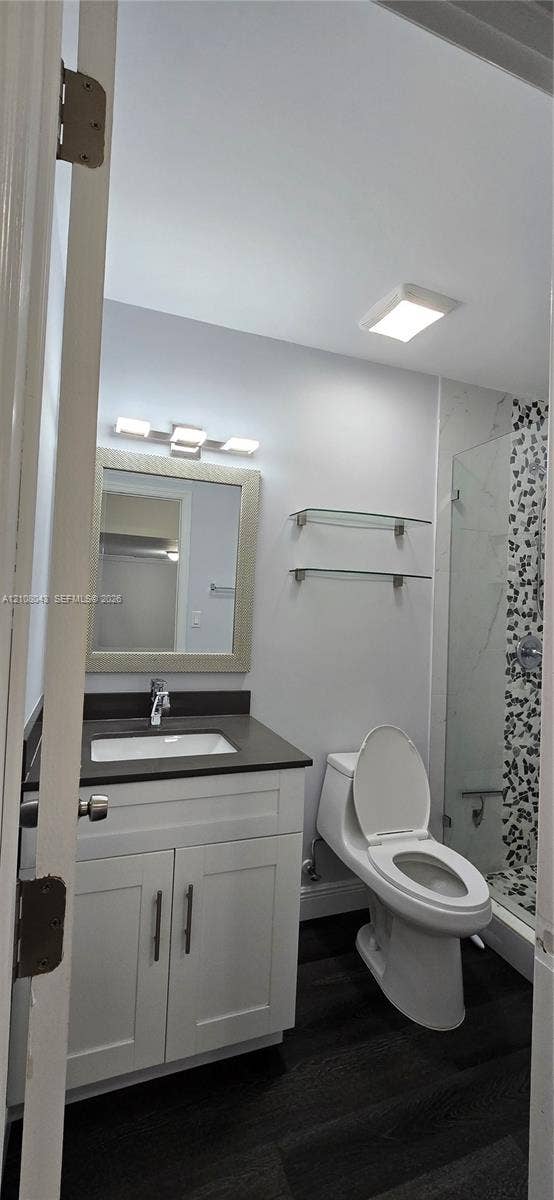 7176 SW 12th Street, #7176, Miami, Miami, FL 33144 Bathroom featuring a white shaker-style vanity with a dark countertop, undermount sink, glass wall-mounted shelving, and wood-finish flooring