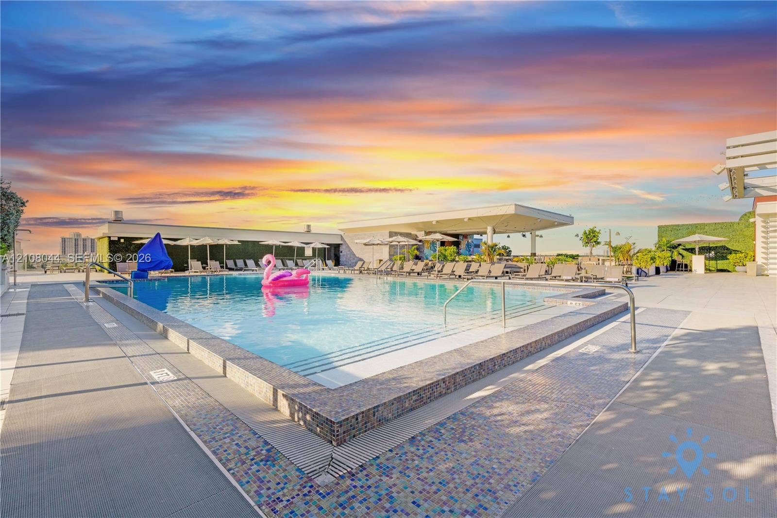 Rooftop swimming pool with tile-accented surround, metal safety railings, concrete decking, and covered structural canopy