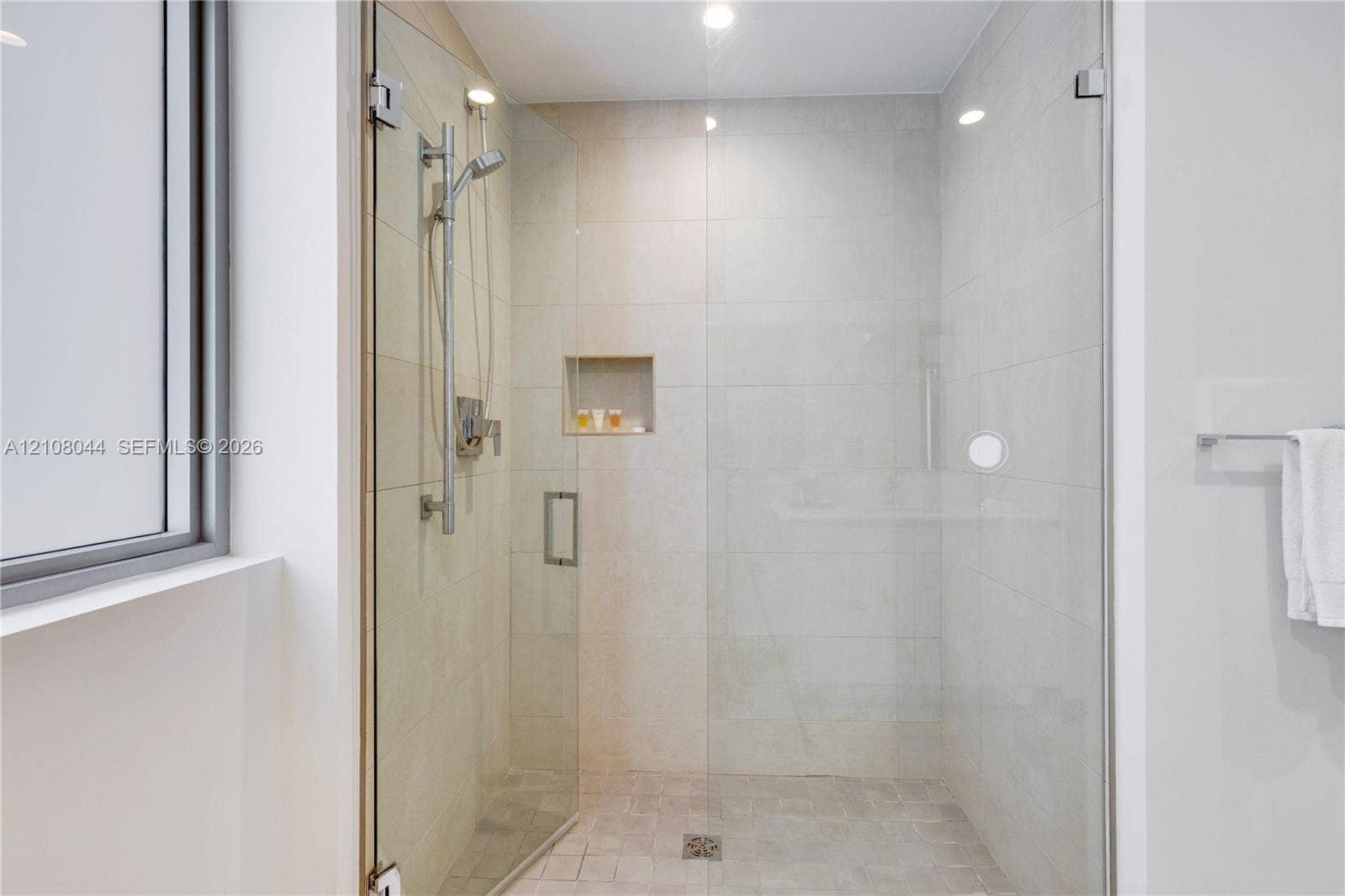 Walk-in shower featuring large-format wall tile, glass enclosure, built-in recessed niche, adjustable hand-held shower head, and recessed ceiling lighting