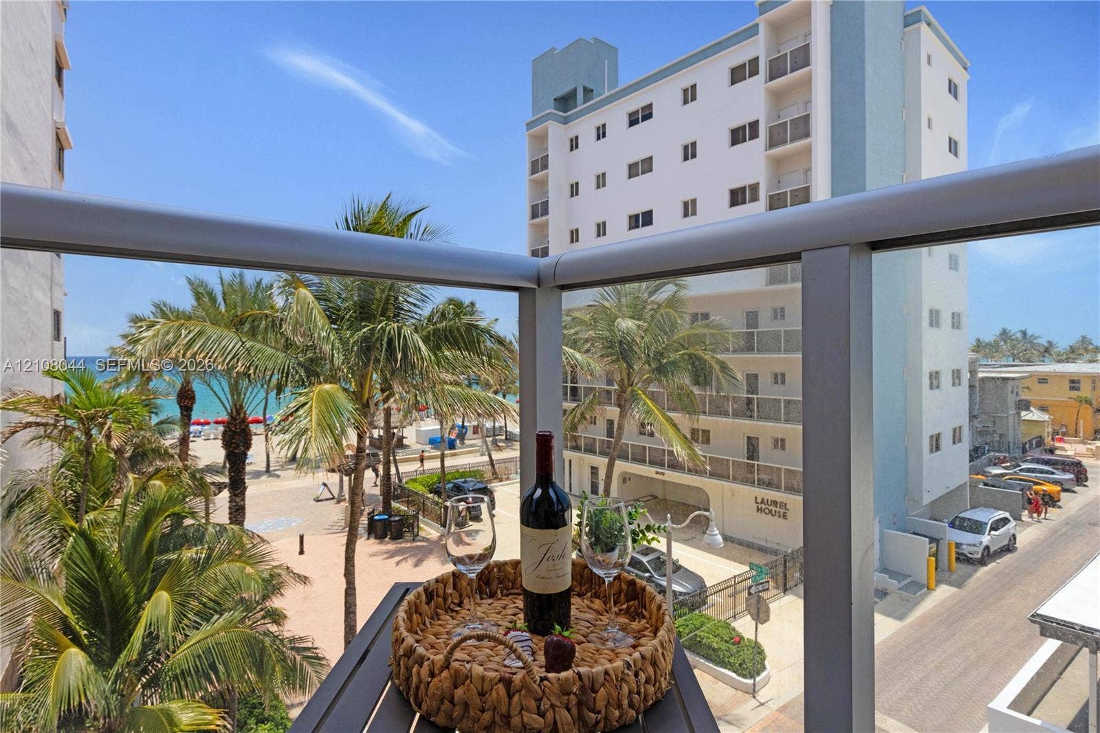 Private balcony featuring a metal frame and glass railing overlooking coastal scenery and palm trees