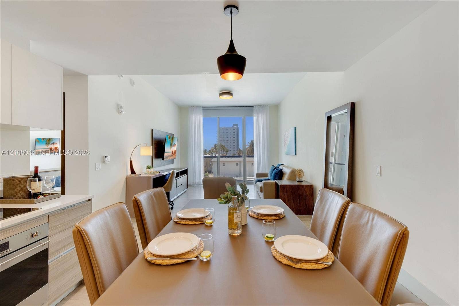 Kitchen area with built-in cabinetry, stainless steel oven, and light-toned wood-finish cabinetry, complemented by a hanging pendant light fixture and floor-to-ceiling glass doors