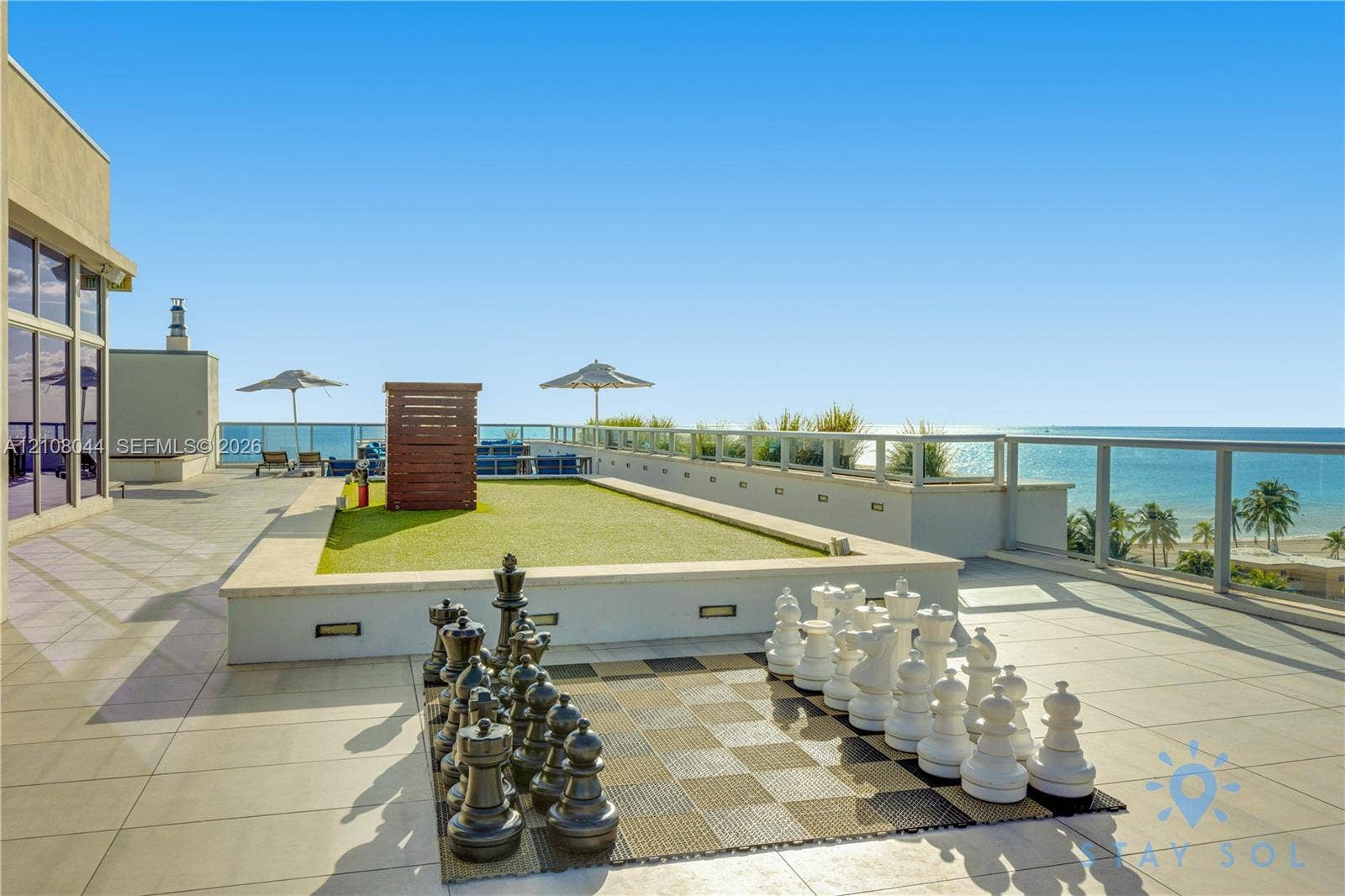 Expansive rooftop terrace featuring large-format stone tile flooring, a raised artificial turf area, integrated low-voltage landscape lighting, and a glass-panel railing system