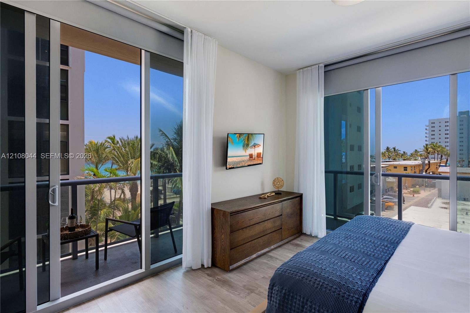 Floor-to-ceiling glass sliding doors, wood-finish flooring, and dual private balconies with metal railings