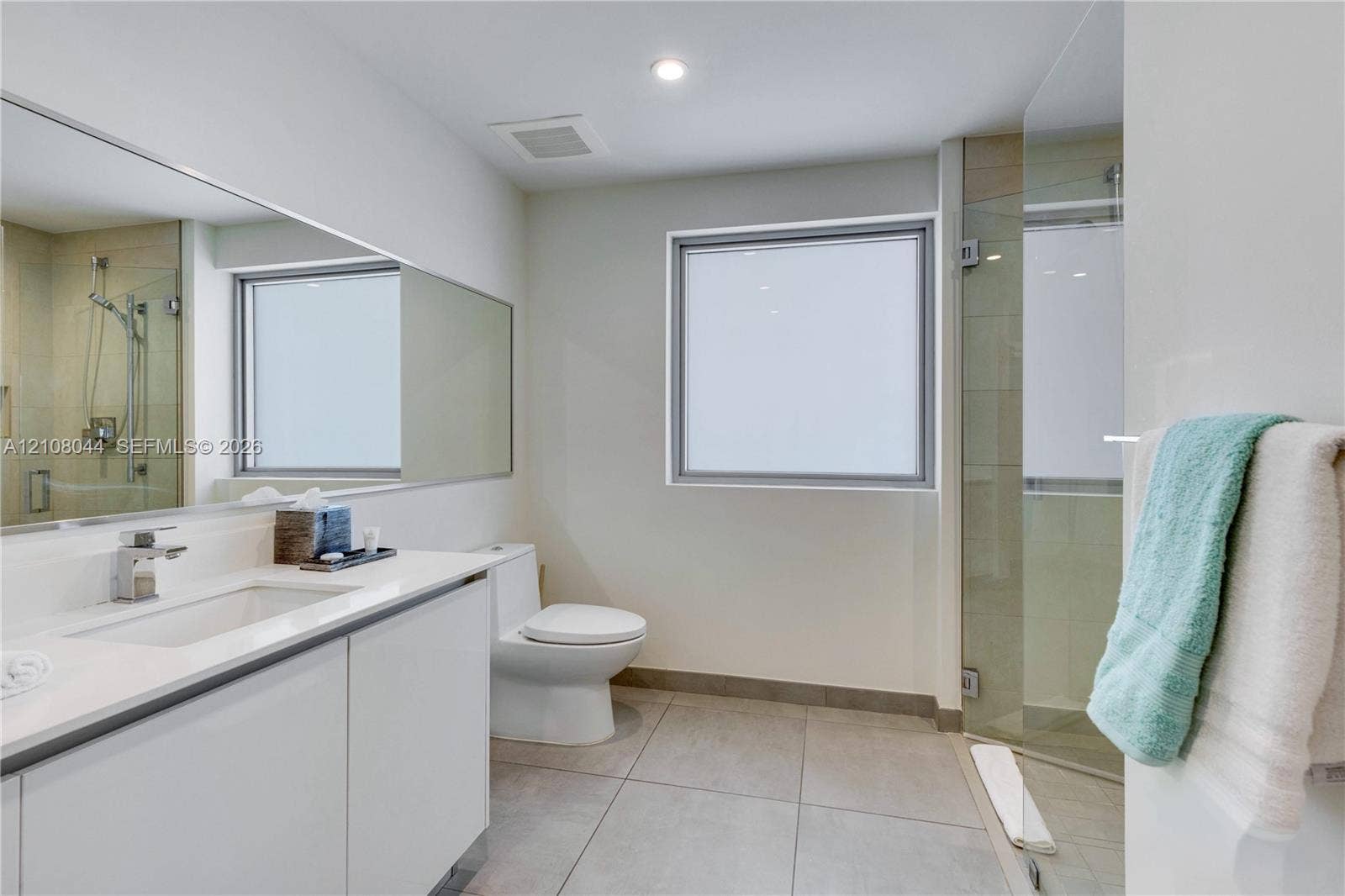 Bathroom featuring a vanity with a white countertop and rectangular undermount sink, a large wall-mounted mirror, a walk-in shower with a glass door, and large-format tile flooring