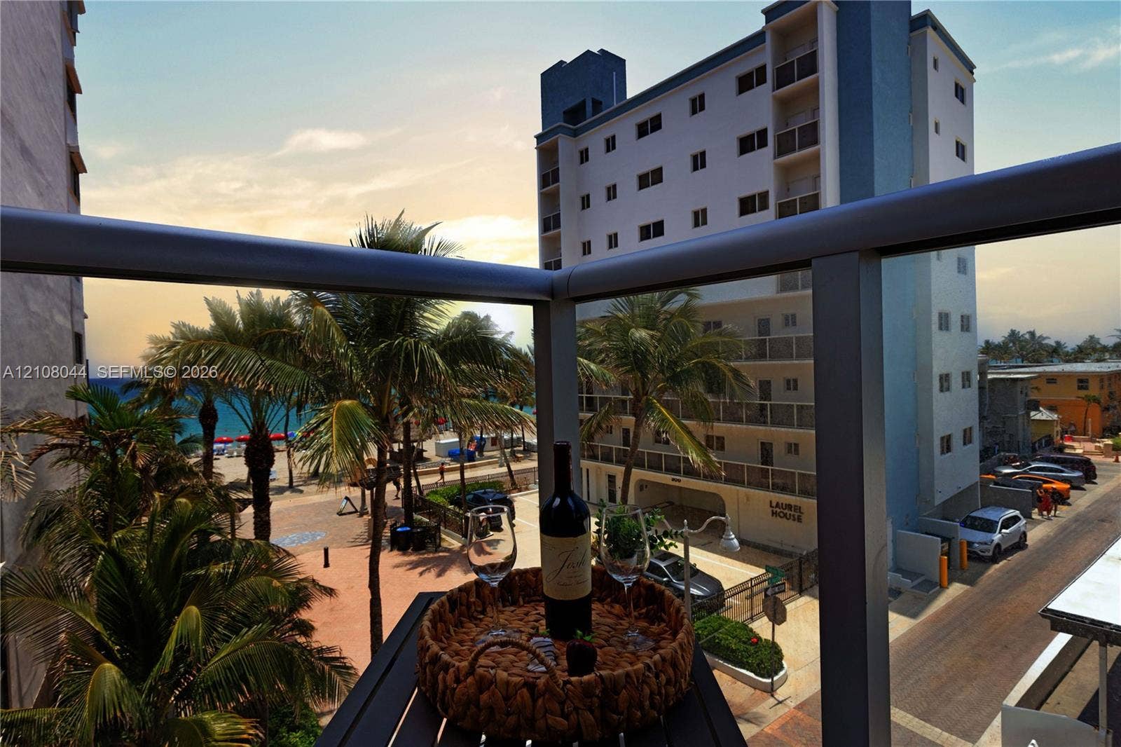 Elevated balcony with a metal and glass railing, featuring an ocean-facing orientation and palm tree scenery