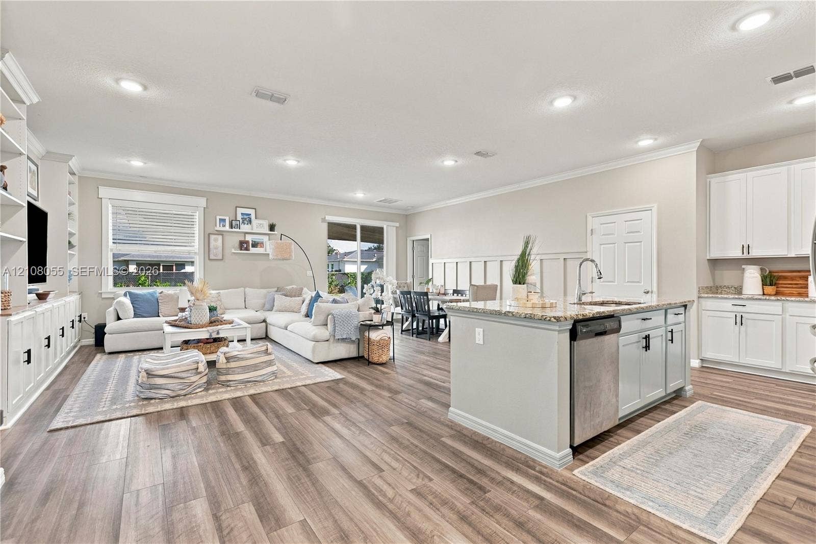 557 SW Lacroix Avenue, Port St Lucie, FL 34953 Open-concept area featuring wood-finish flooring, recessed lighting, built-in cabinetry, an island with a stone-finish countertop, and decorative wall paneling