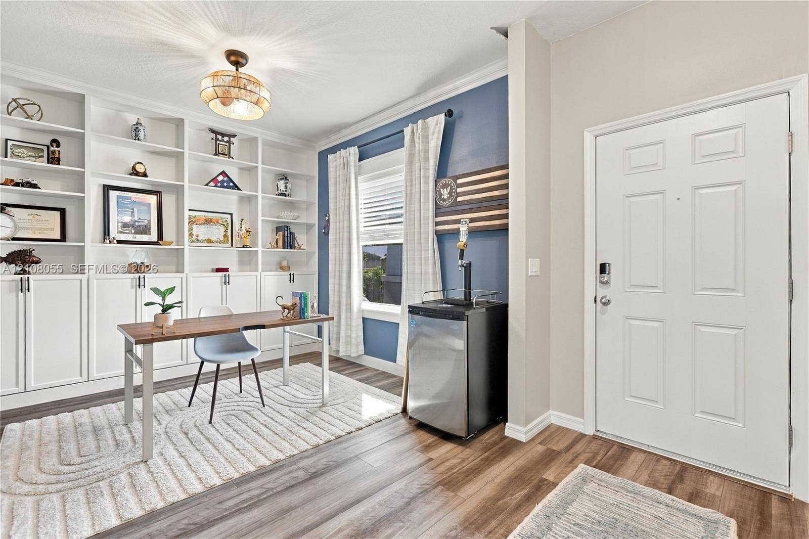 557 SW Lacroix Avenue, Port St Lucie, FL 34953 Built-in floor-to-ceiling white shelving with lower cabinetry, wood-finish flooring, multi-pane window with trim, decorative ceiling-mounted fixture, and a six-panel entry door