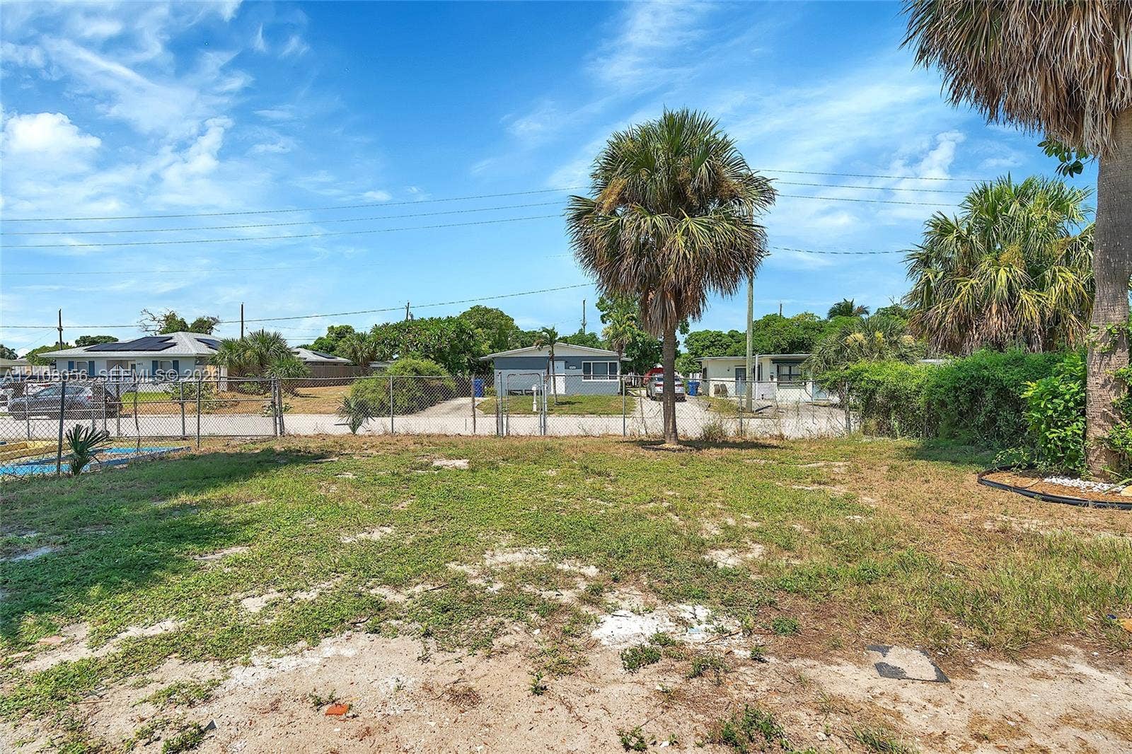 1444 W 28th Street, Riviera Beach, FL 33404 Expansive lot featuring mature palm trees and chain-link perimeter fencing