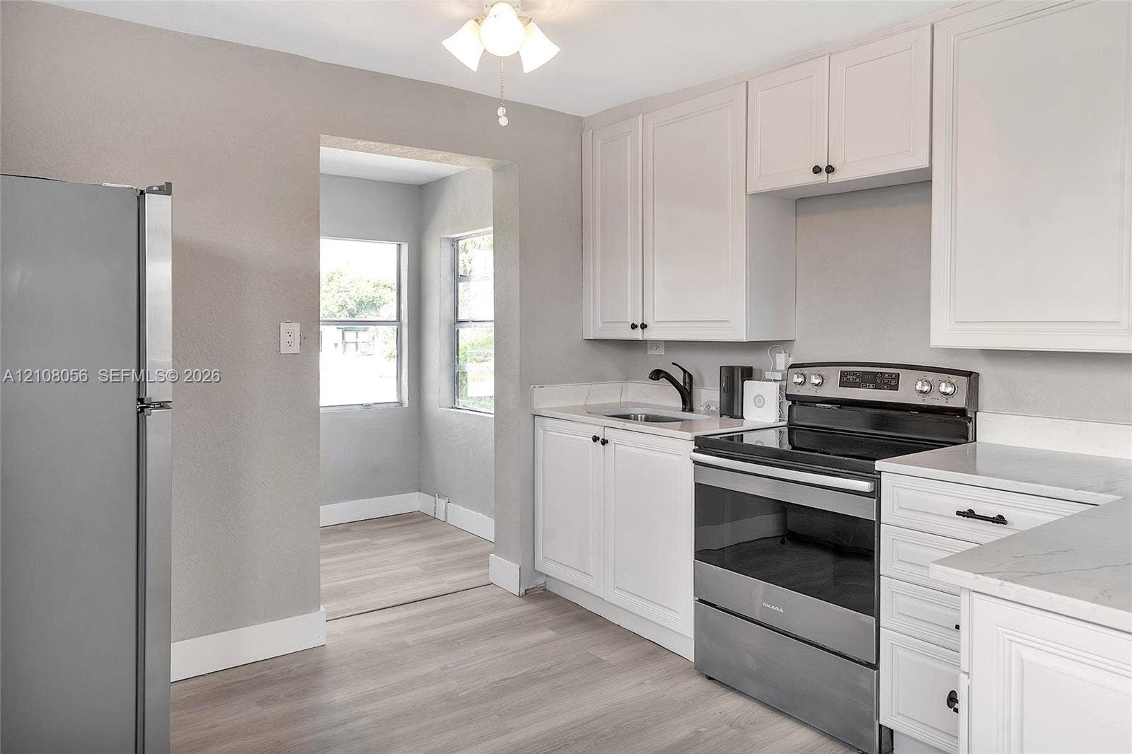 1444 W 28th Street, Riviera Beach, FL 33404 Kitchen featuring white shaker-style cabinetry, stainless steel appliances, light-toned stone-finish countertops, and wood-finish flooring