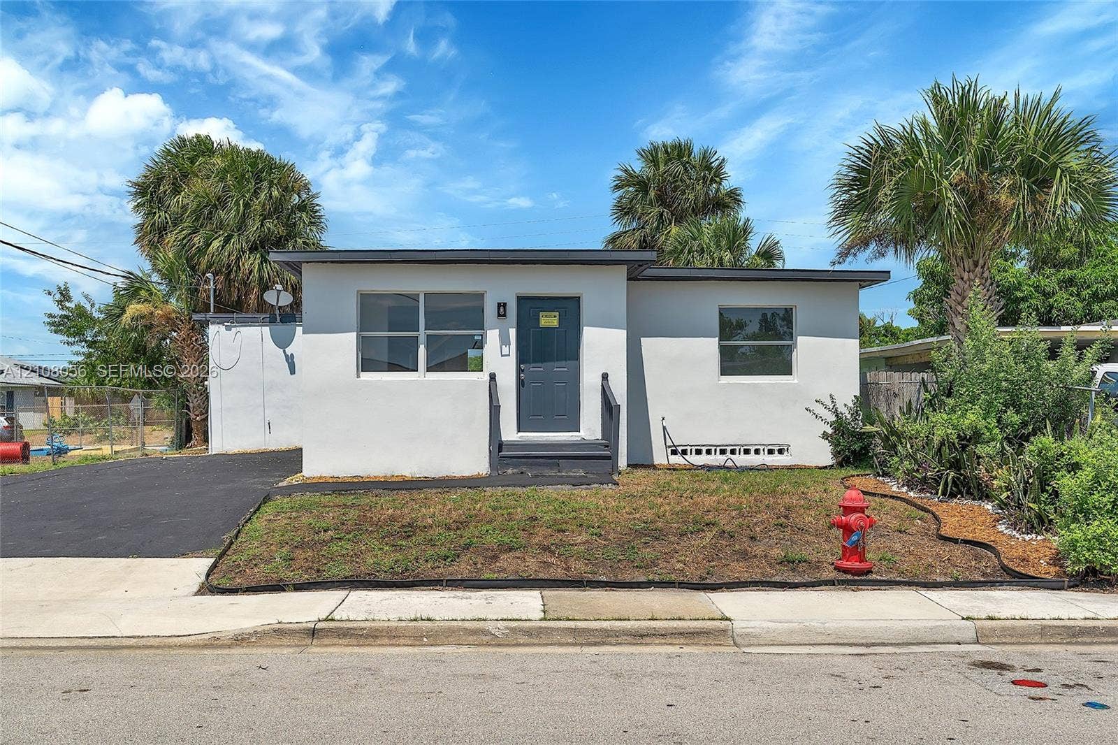 1444 W 28th Street, Riviera Beach, FL 33404 Single-story exterior featuring light-toned stucco siding, a flat roofline, an asphalt-paved driveway, and a front entry landing with dark-toned stairs