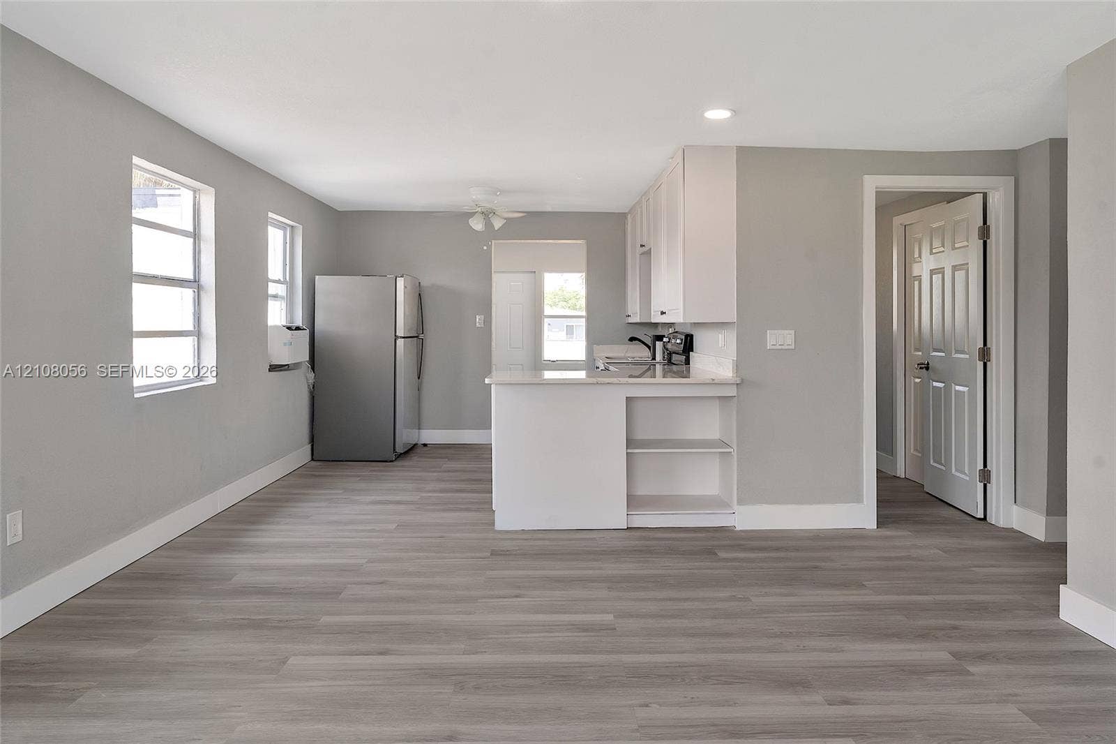 1444 W 28th Street, Riviera Beach, FL 33404 Kitchen area featuring white cabinetry, a peninsula with built-in shelving, wood-finish flooring, recessed lighting, and stainless steel refrigerator