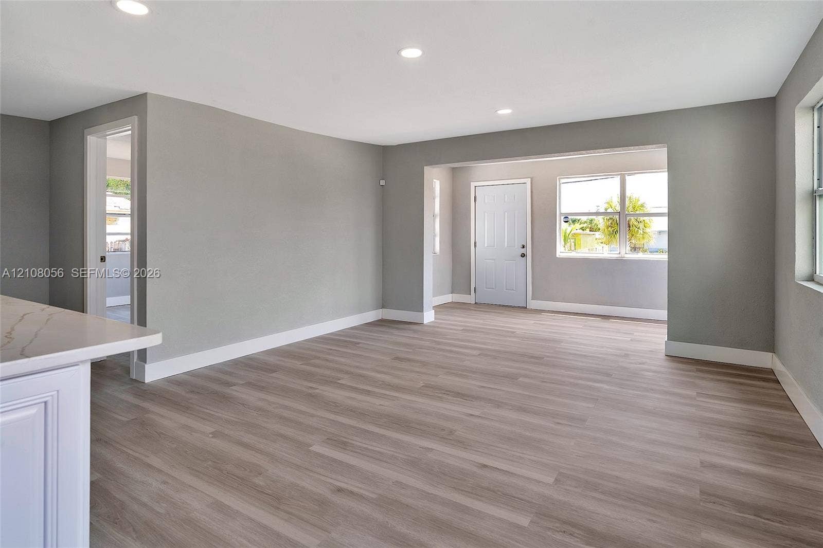 1444 W 28th Street, Riviera Beach, FL 33404 Open-concept living space featuring wood-finish flooring, recessed lighting, white cabinetry with a light-toned stone-finish countertop, and windows with natural light