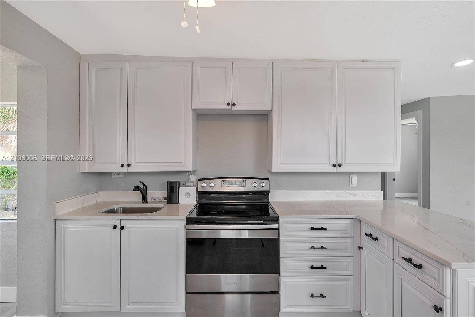1444 W 28th Street, Riviera Beach, FL 33404 Kitchen featuring white shaker-style cabinetry, light-toned stone countertops, stainless steel electric range, undermount sink with a matte black faucet, and coordinating matte black hardware