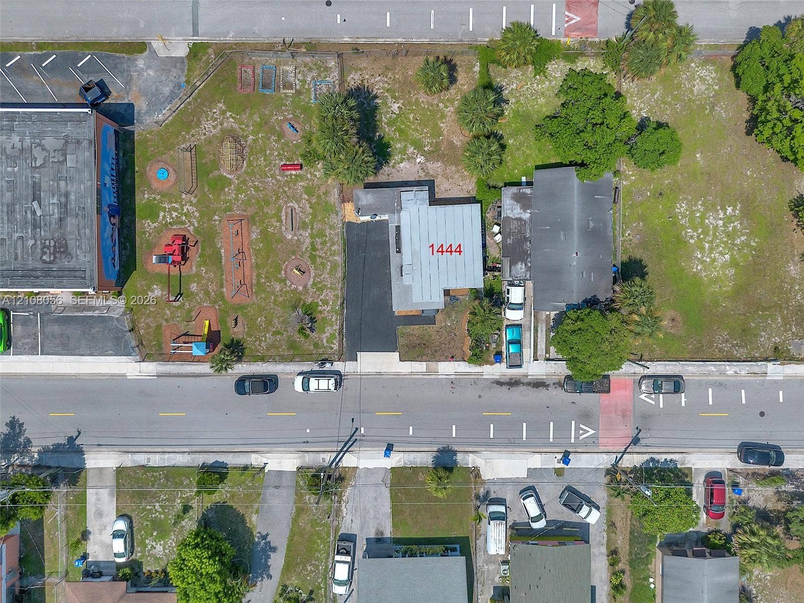 1444 W 28th Street, Riviera Beach, FL 33404 Aerial perspective of a property featuring an asphalt driveway, paved exterior areas, and surrounding mature trees