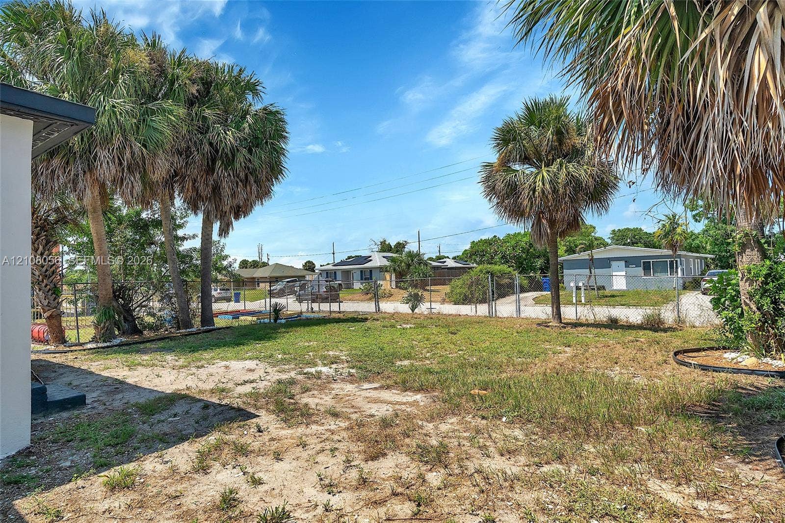1444 W 28th Street, Riviera Beach, FL 33404 Open-space backyard featuring mature palm trees, perimeter chain-link fencing, and a combination of grass and sand ground cover