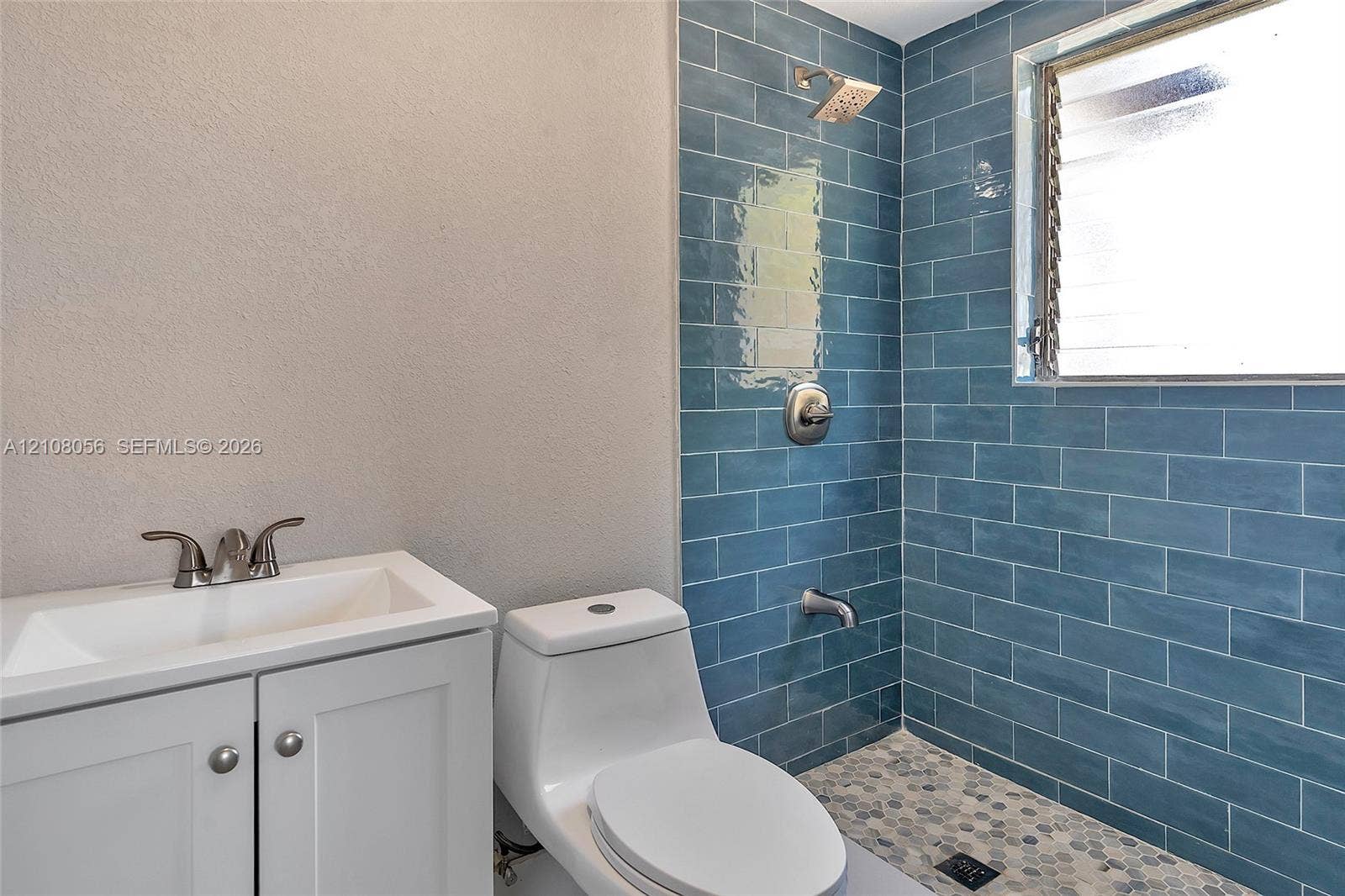 1444 W 28th Street, Riviera Beach, FL 33404 Bathroom featuring blue subway wall tile, pebble-stone flooring, white cabinetry, integrated sink, and polished chrome fixtures