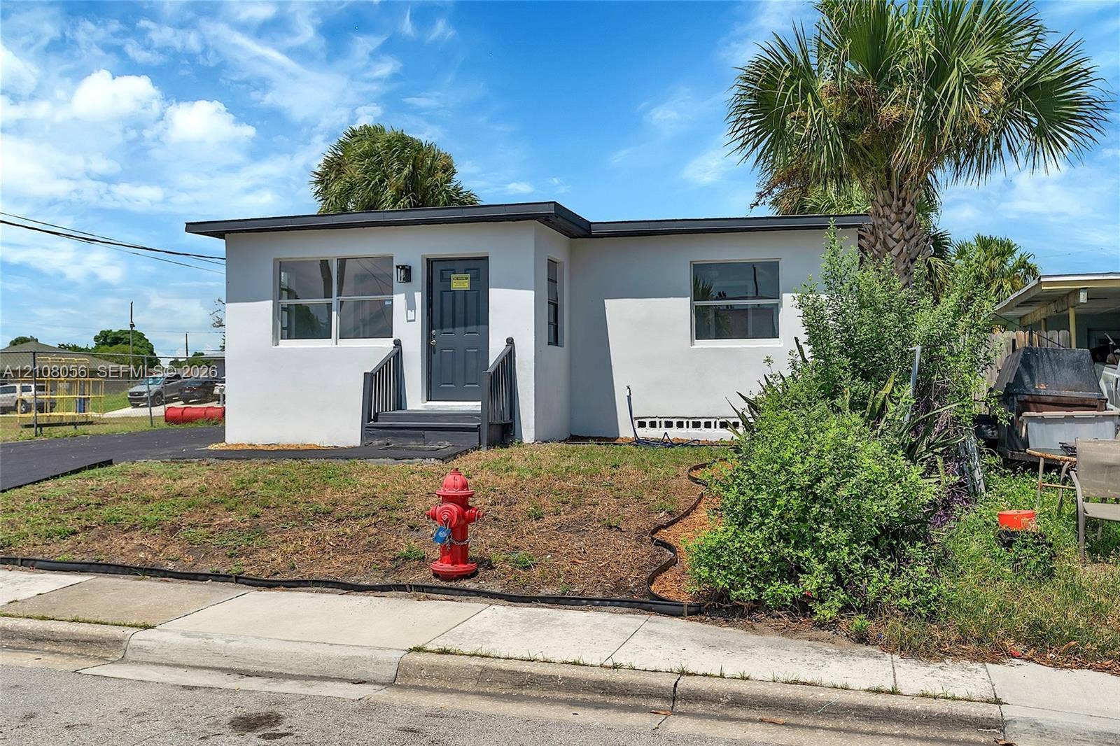 1444 W 28th Street, Riviera Beach, FL 33404 Single-story exterior featuring a white stucco facade, flat roofline, dark-toned entry door, and paved driveway