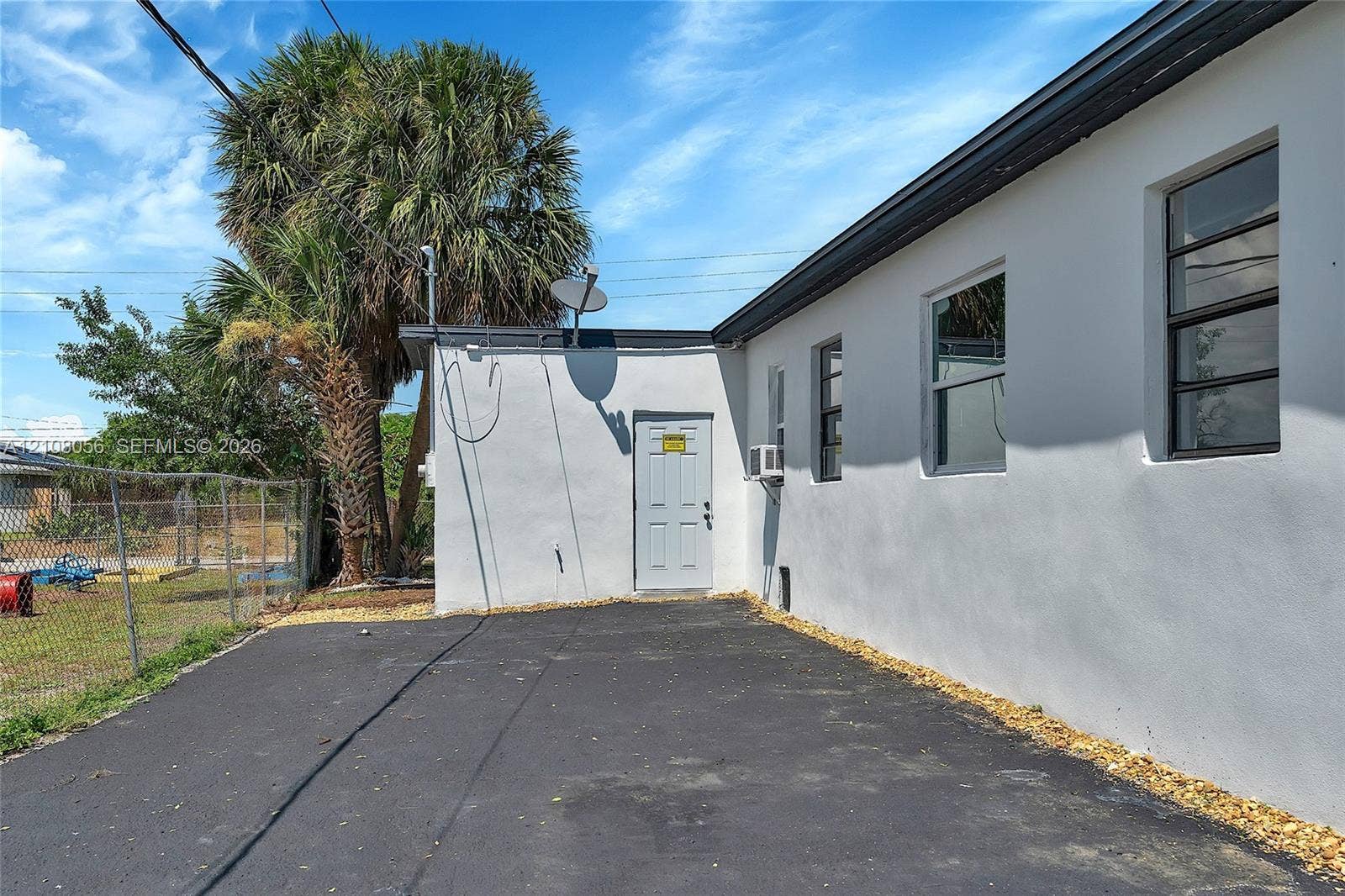 1444 W 28th Street, Riviera Beach, FL 33404 Exterior features include smooth white stucco siding, asphalt paving, and a fenced perimeter
