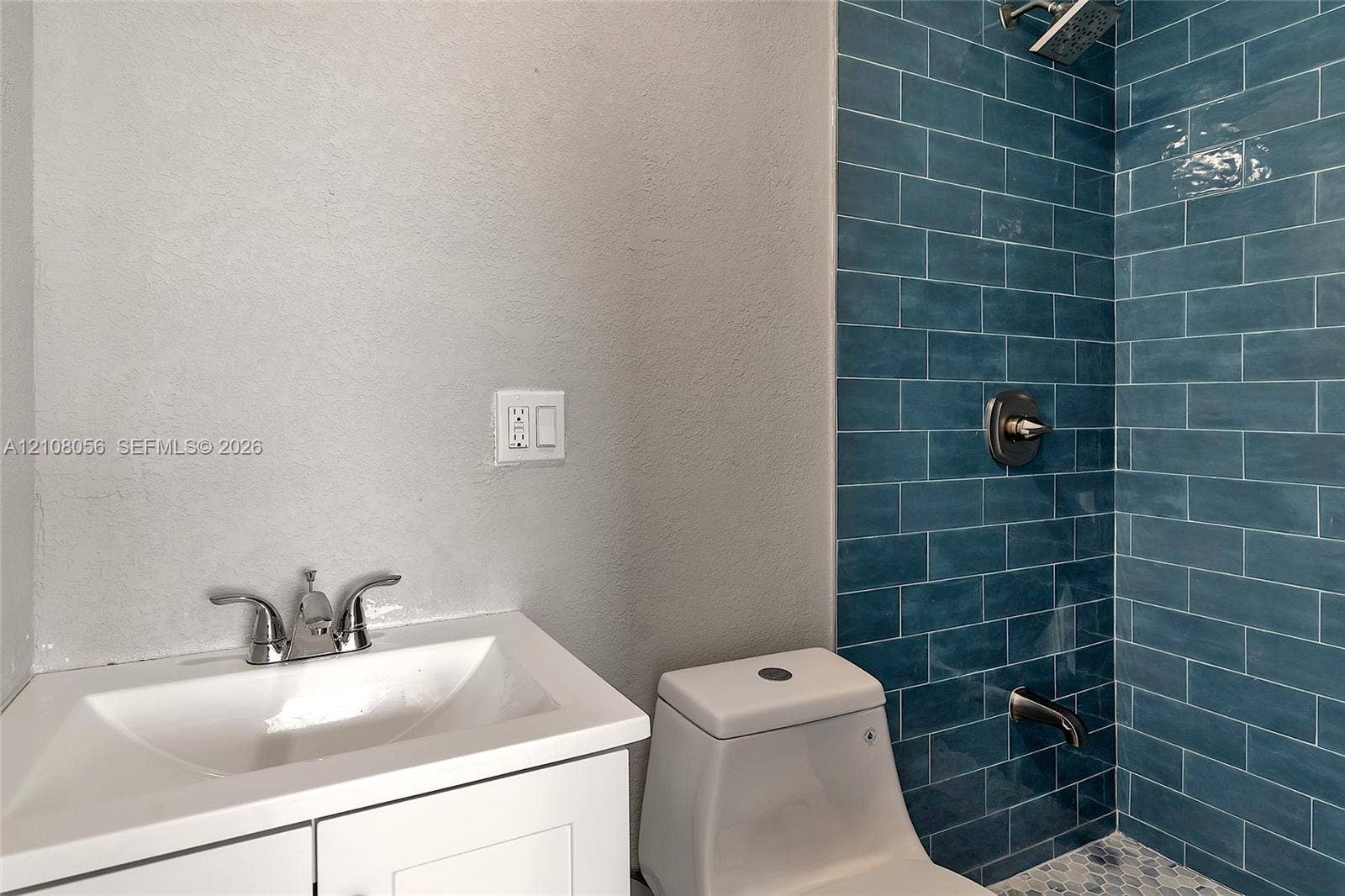 1444 W 28th Street, Riviera Beach, FL 33404 White vanity cabinet with an integrated basin, chrome dual-handle faucet, one-piece toilet, and blue subway-tiled shower surround with chrome fixtures