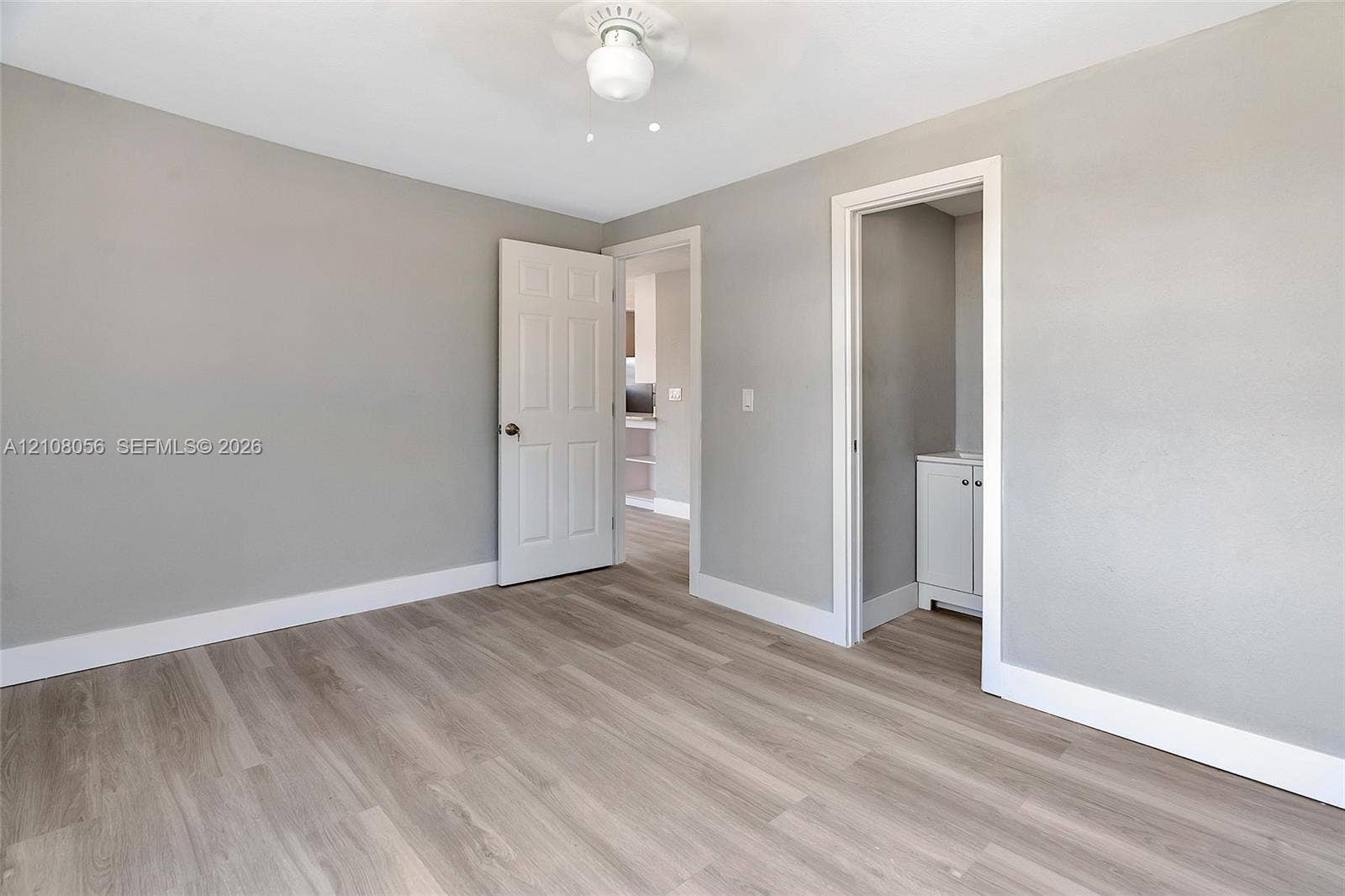 1444 W 28th Street, Riviera Beach, FL 33404 Neutral-toned interior space featuring wood-finish flooring, a ceiling fan with integrated lighting, and a six-panel door