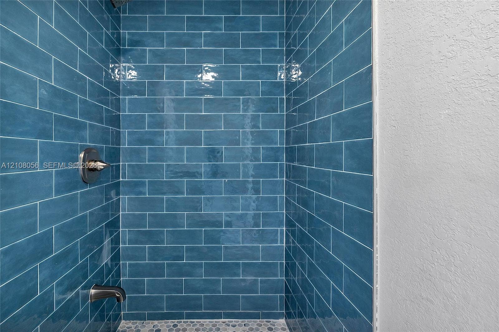 1444 W 28th Street, Riviera Beach, FL 33404 Shower enclosure featuring blue subway tile walls, a pebble-finish floor, and metallic hardware