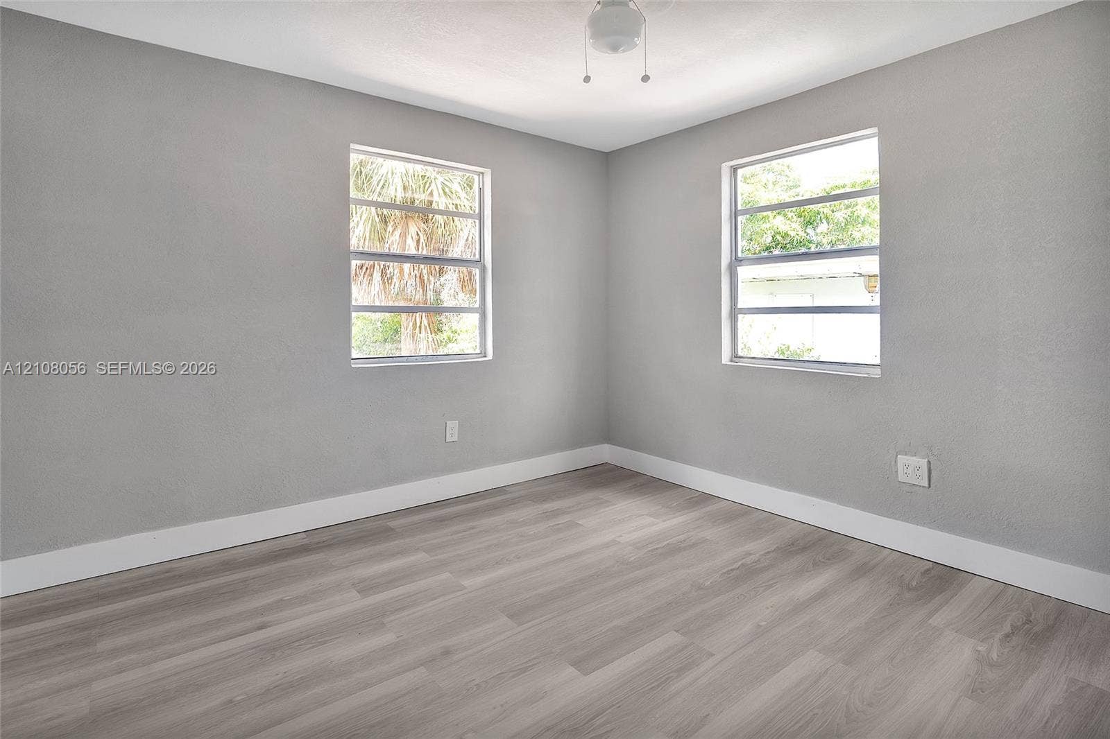 1444 W 28th Street, Riviera Beach, FL 33404 Neutral-toned interior space featuring wood-finish flooring, two horizontal sliding windows, and a central ceiling-mounted light fixture