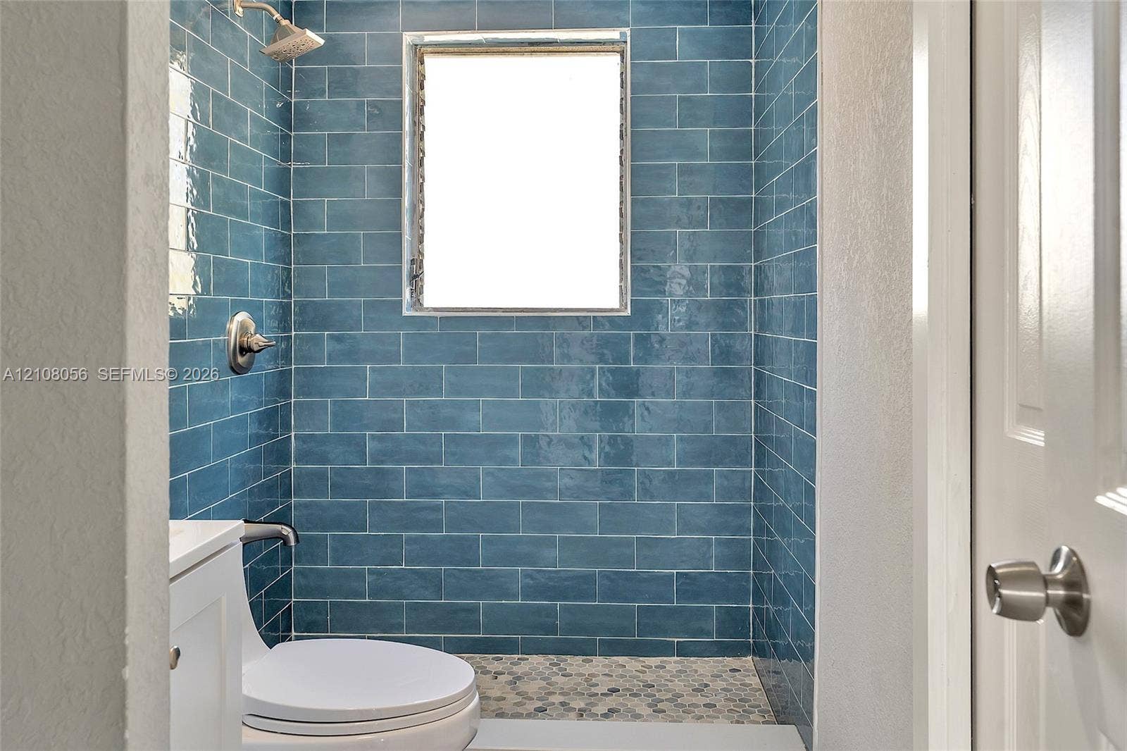 1444 W 28th Street, Riviera Beach, FL 33404 Walk-in shower featuring glossy blue subway tile, a natural stone pebble floor, a built-in shower head, and a privacy window