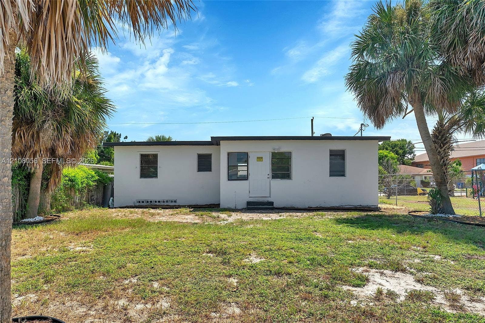 1444 W 28th Street, Riviera Beach, FL 33404 Exterior featuring a flat-roof structure with stucco siding, multiple windows, and mature palm trees