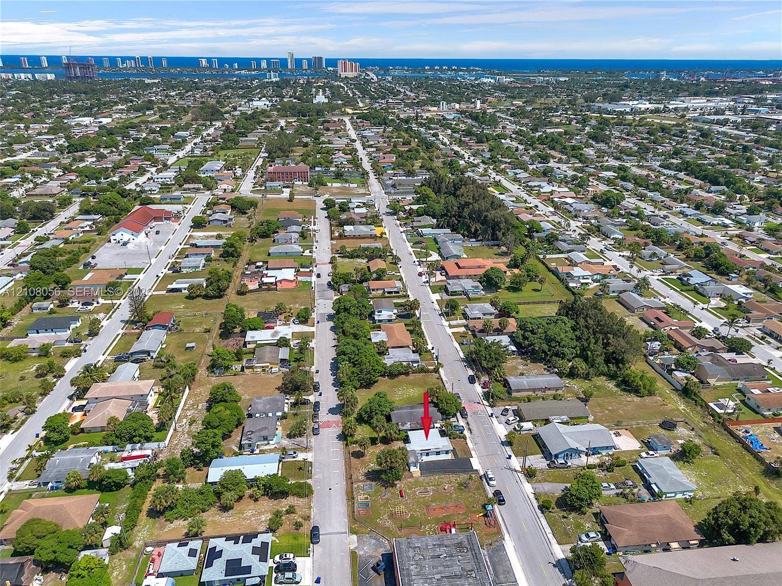 1444 W 28th Street, Riviera Beach, FL 33404 Aerial perspective of a corner lot property featuring an asphalt-shingled roof and exterior hardscaping, situated in proximity to coastal waterfront and urban infrastructure
