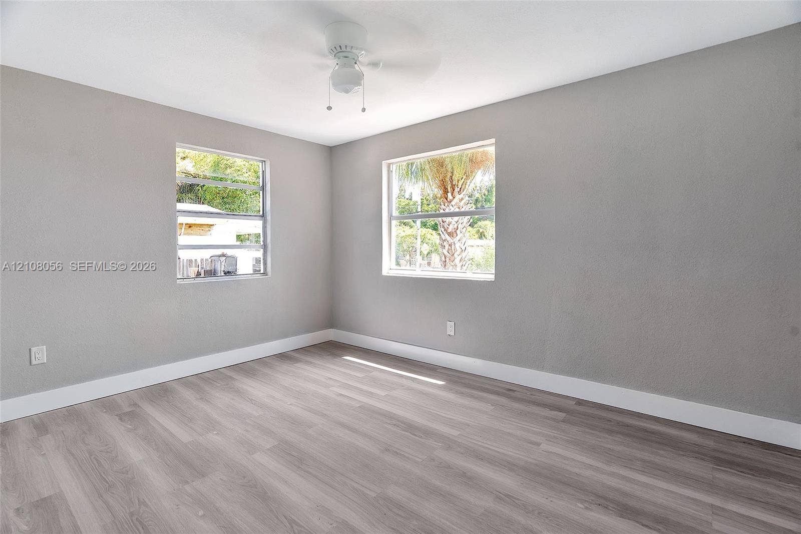 1444 W 28th Street, Riviera Beach, FL 33404 Neutral-toned interior space featuring wood-finish flooring, dual windows, and a ceiling-mounted light fixture with fan