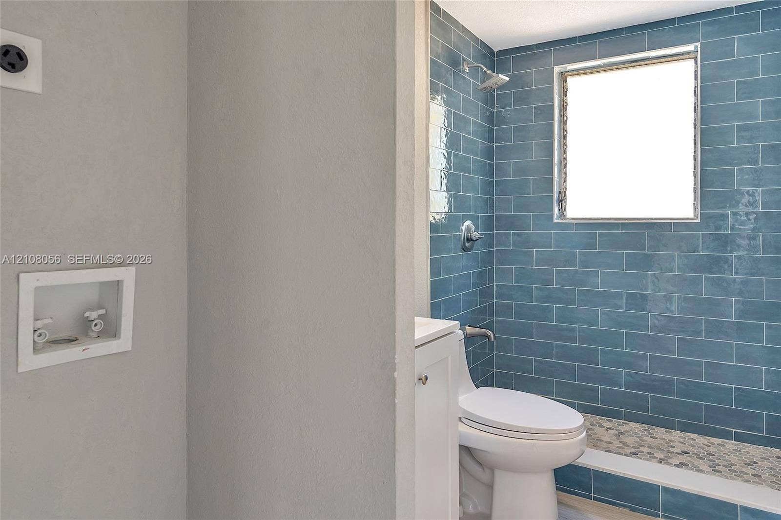 1444 W 28th Street, Riviera Beach, FL 33404 Bathroom featuring blue subway wall tile, pebble-stone shower flooring, a wall-mounted shower fixture, an integrated laundry hookup box, and a white pedestal vanity