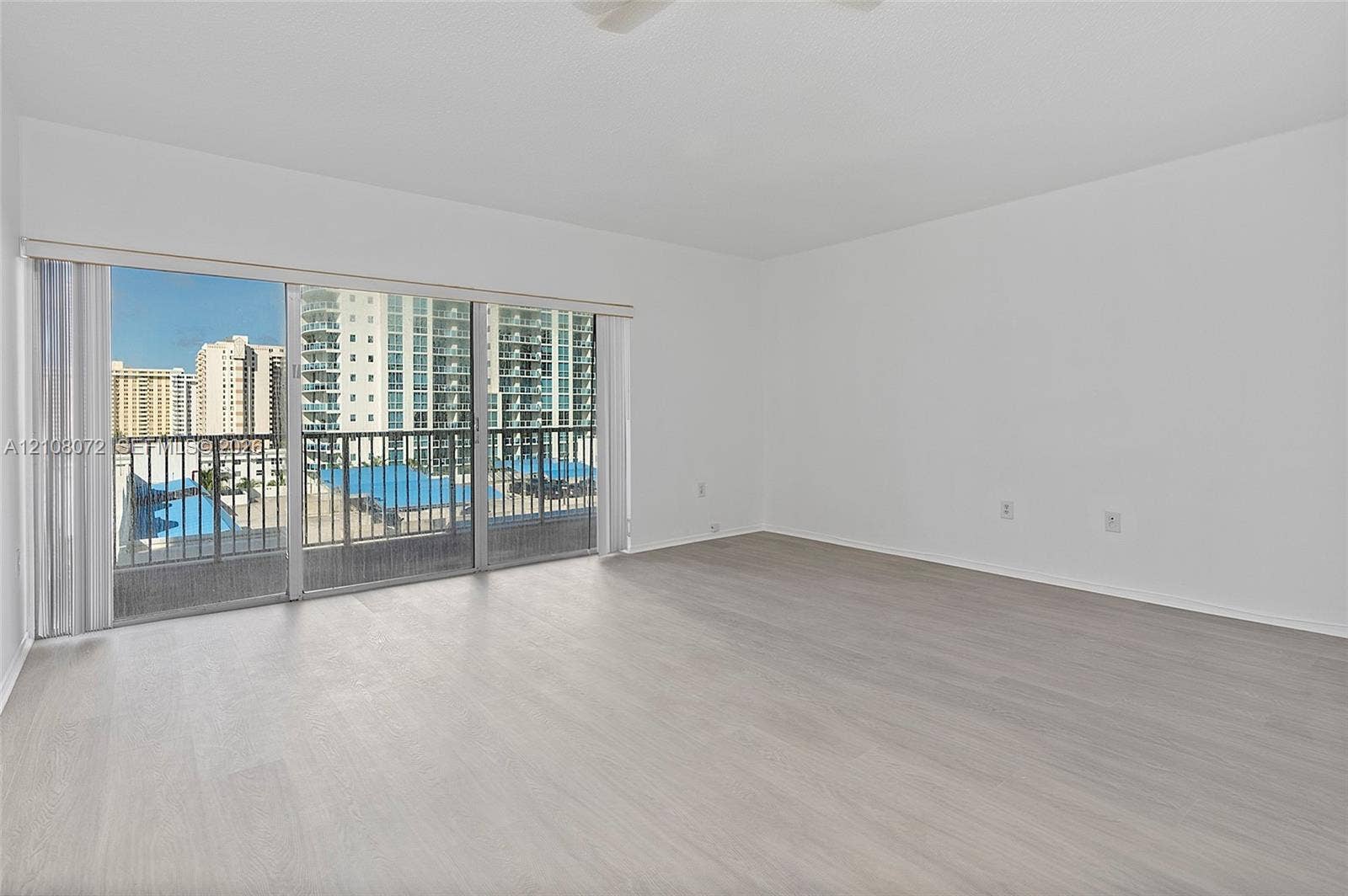 Open-concept interior featuring light wood-finish flooring, sliding glass balcony doors, and a metal-railed balcony