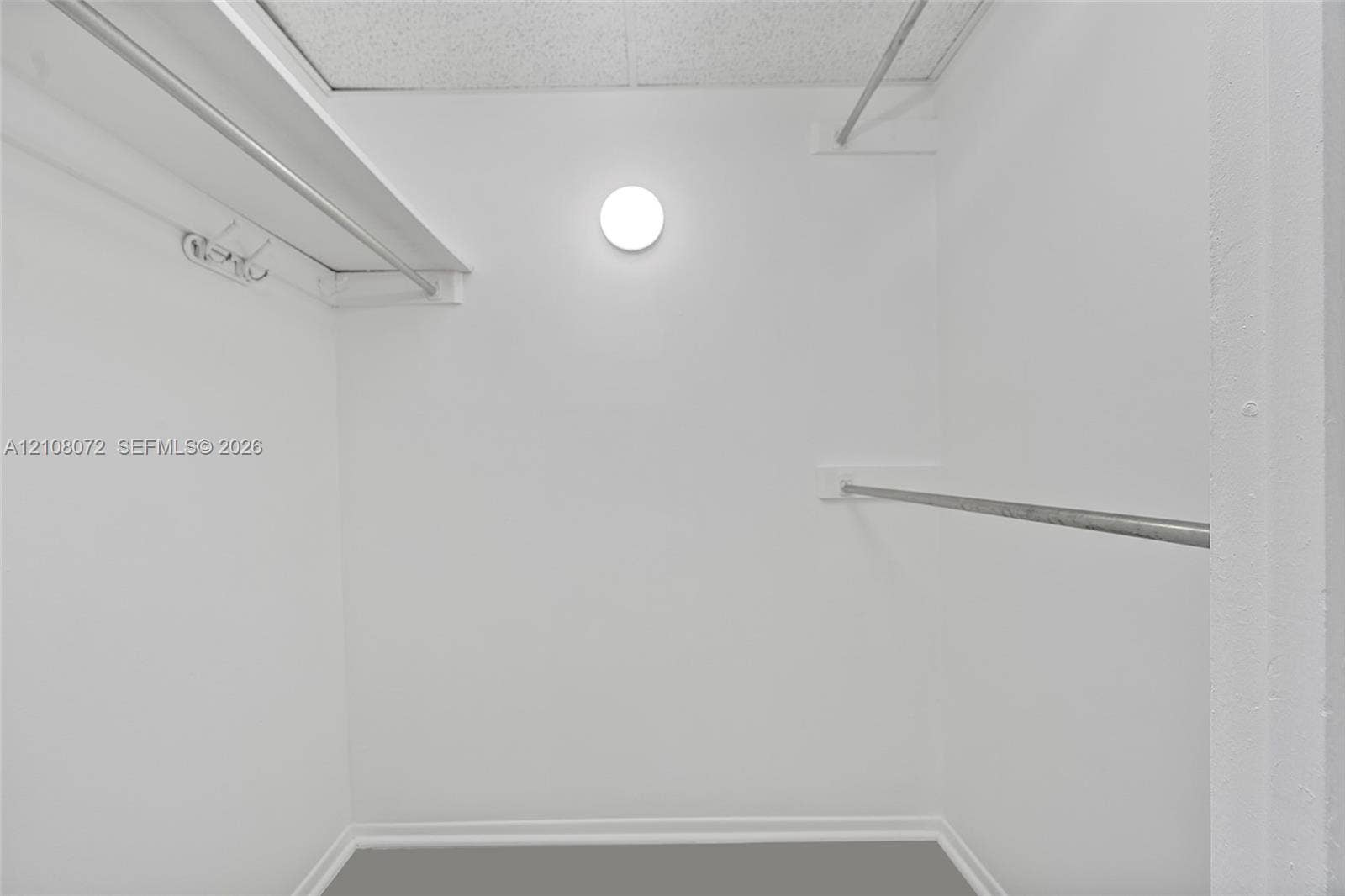 Walk-in closet featuring dual metal hanging rods, tiered shelving, and a wall-mounted circular light fixture