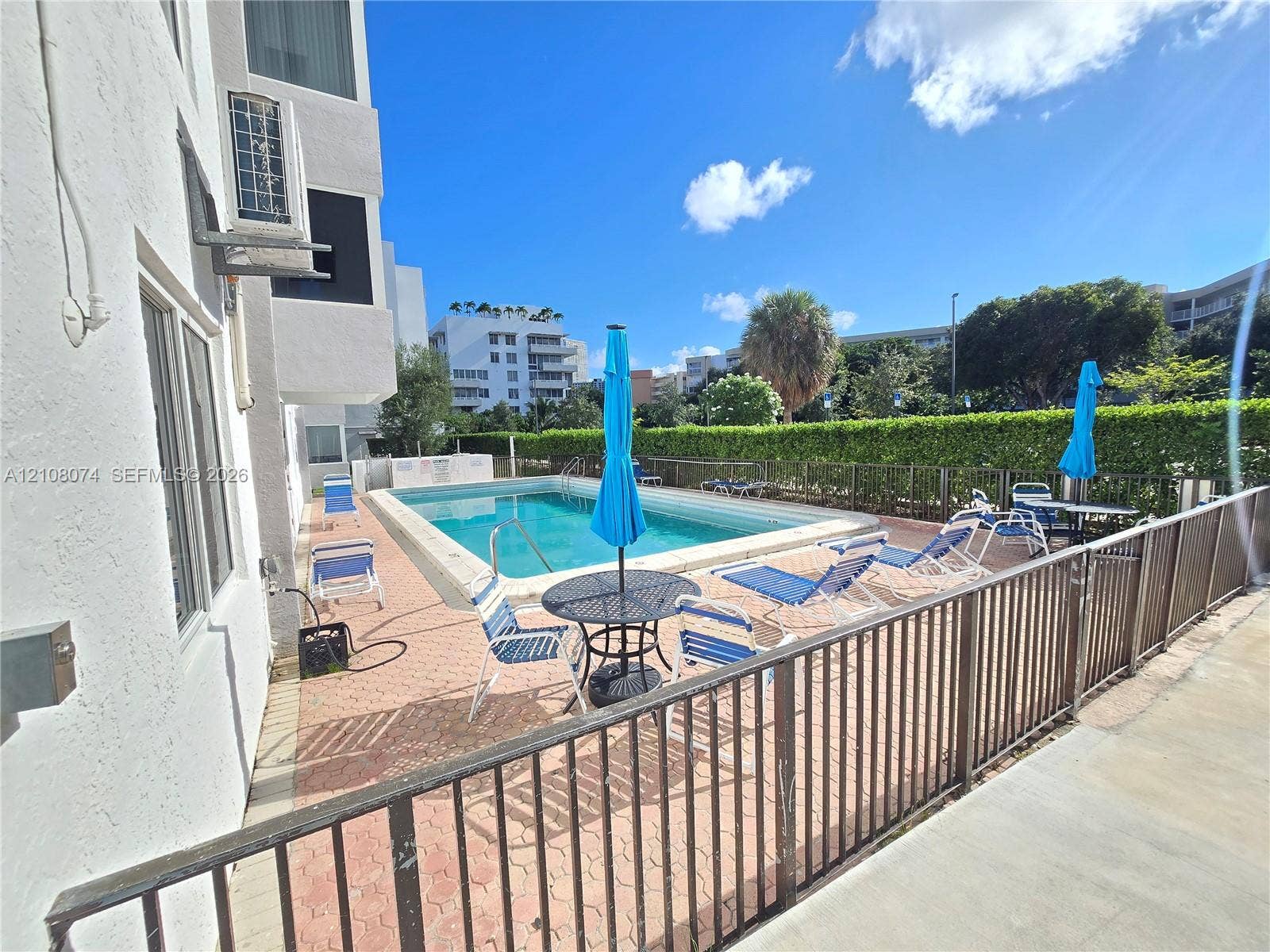 250 180th Drive, #202, Sunny Isles Beach, Sunny Isles Beach, FL 33160 Outdoor swimming pool area featuring a paved deck, metal perimeter fencing, and established perimeter hedging