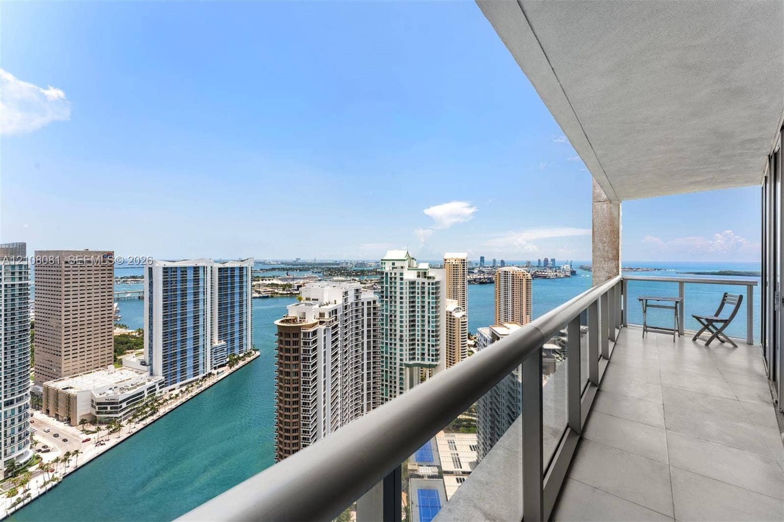 495 Brickell Avenue, #4502, Miami, FL 33131 Covered balcony featuring large-format stone flooring and a glass-paneled railing overlooking the waterway and coastal skyline
