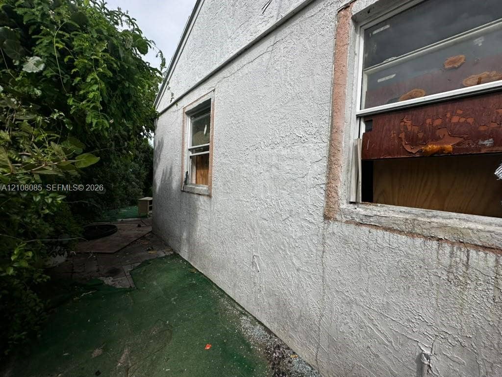Stucco exterior featuring dual window openings and mature perimeter vegetation