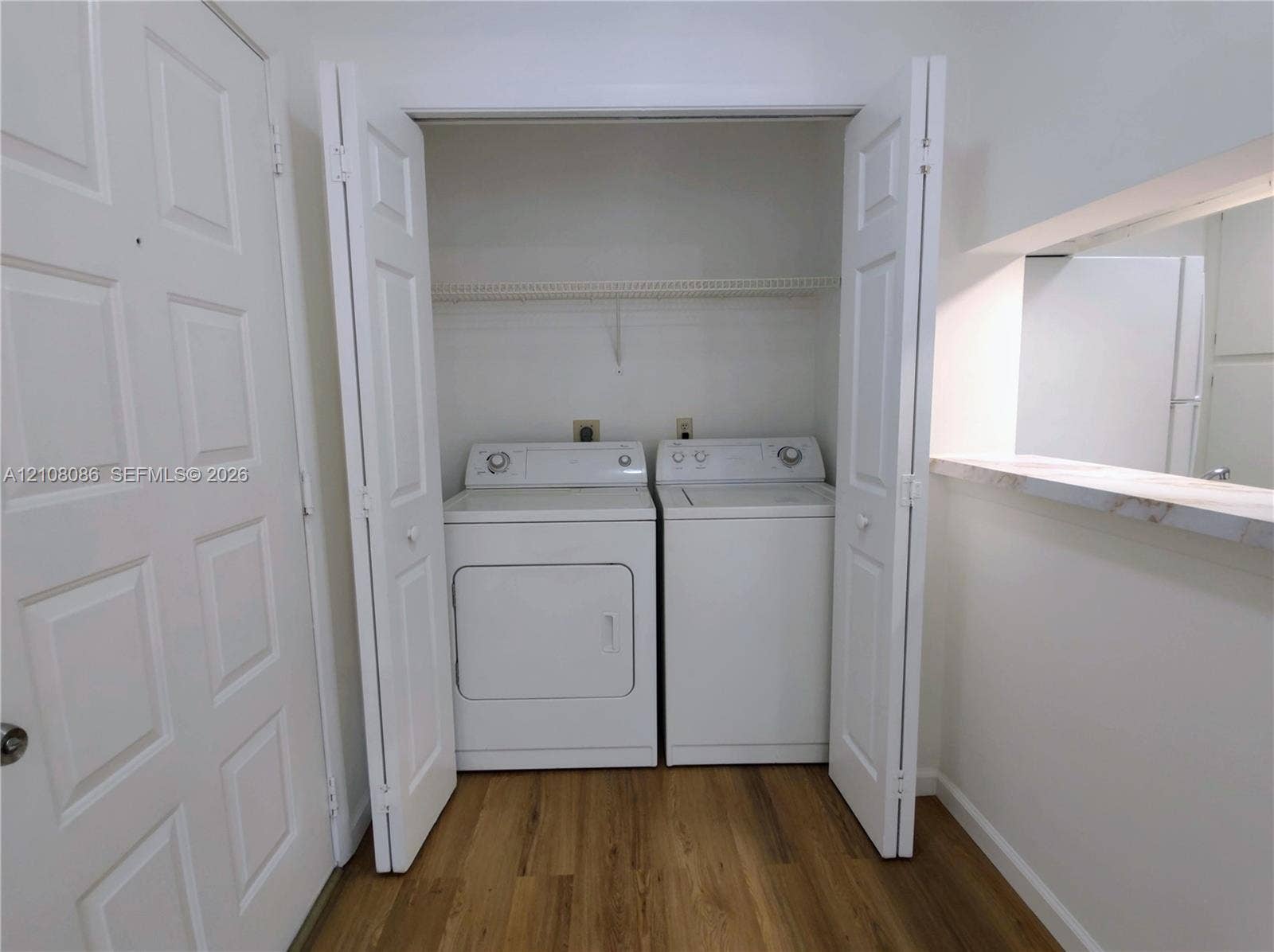 4401 W Mcnab Road, Pompano Beach, FL 33069 Laundry closet featuring bi-fold doors, overhead wire shelving, and wood-finish flooring