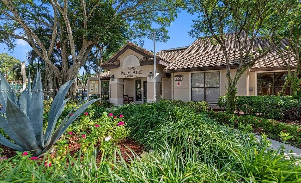 4401 W Mcnab Road, Pompano Beach, FL 33069 Exterior featuring a tiled roof, stucco facade, and lush professional landscaping with mature trees and native greenery