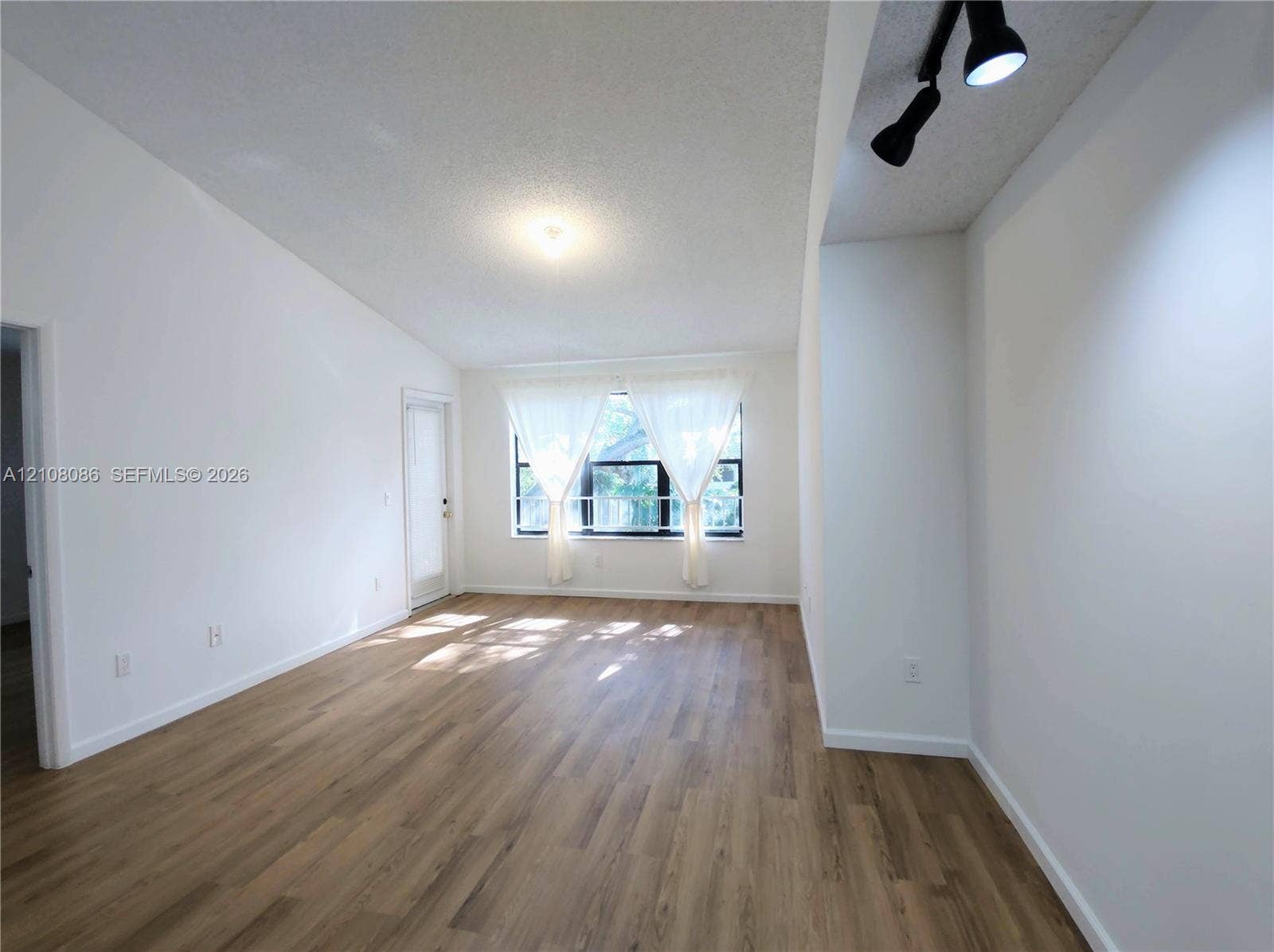 4401 W Mcnab Road, Pompano Beach, FL 33069 Vaulted ceiling featuring neutral wall finishes, wood-finish flooring, multi-pane window, and adjustable track lighting