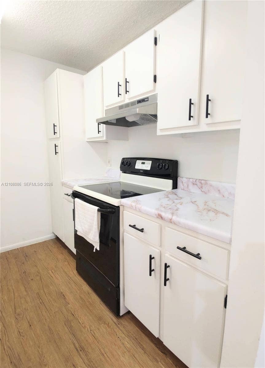 4401 W Mcnab Road, Pompano Beach, FL 33069 Kitchen featuring white cabinetry with matte black hardware, stone-patterned laminate countertops, stainless steel range hood, and wood-finish flooring