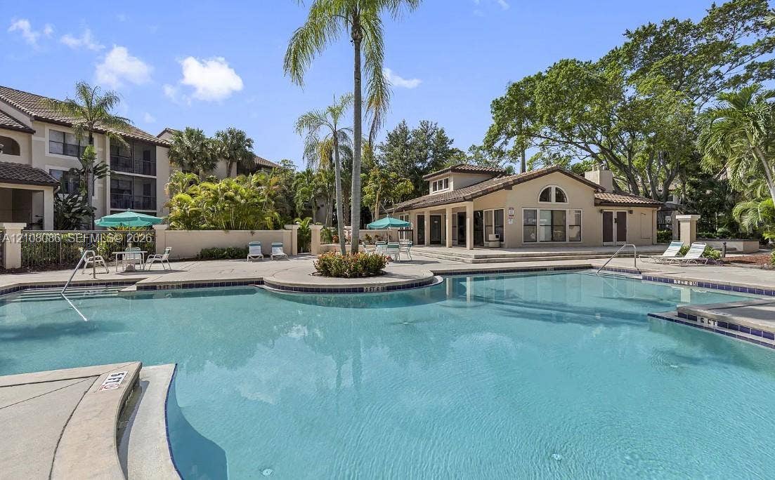 4401 W Mcnab Road, Pompano Beach, FL 33069 Community swimming pool featuring a concrete deck, tiled edge, perimeter wall, and surrounding palm trees