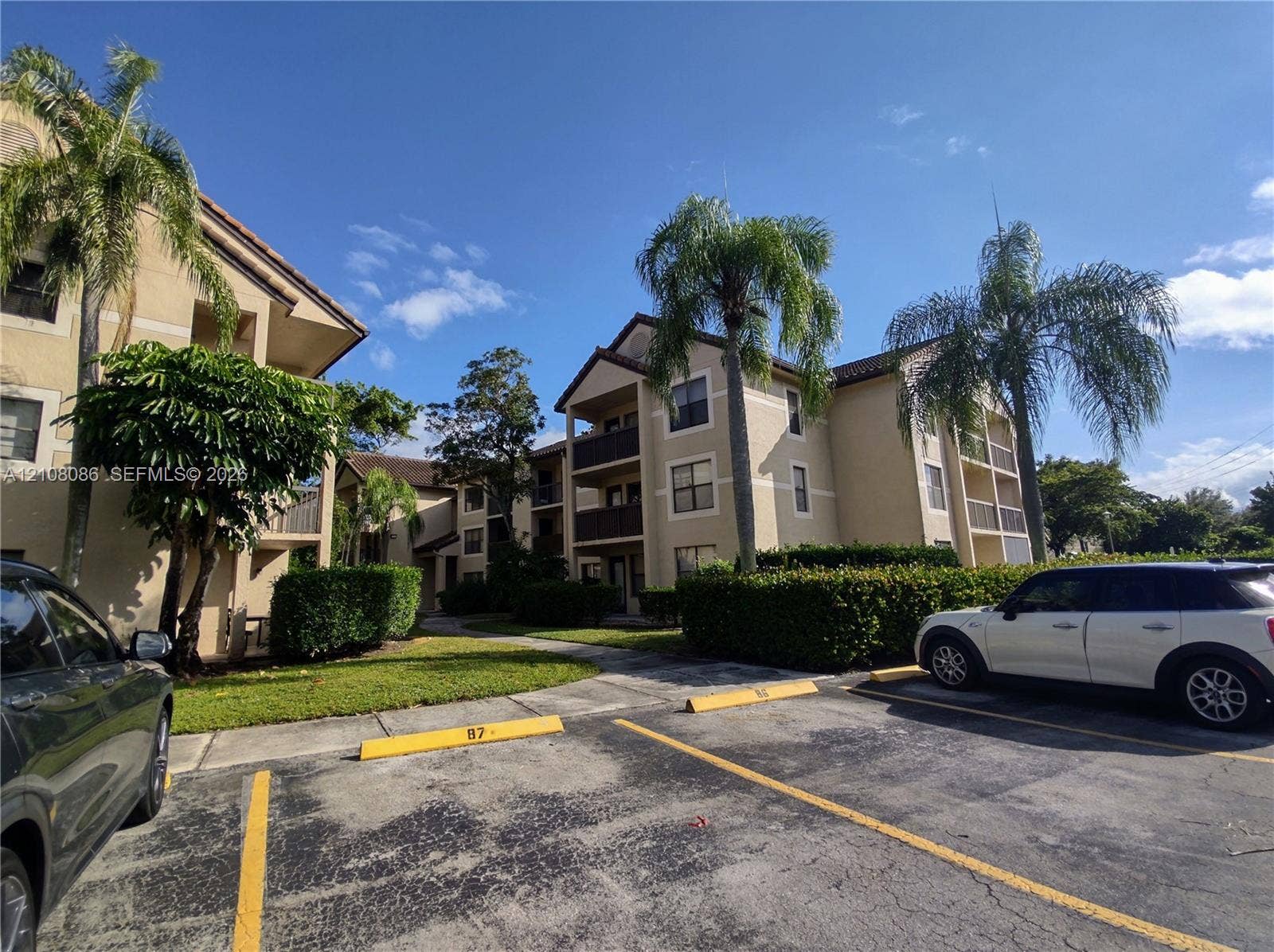 4401 W Mcnab Road, Pompano Beach, FL 33069 Multi-story residential building exterior featuring stucco siding, gabled rooflines, recessed balconies, and mature palm trees